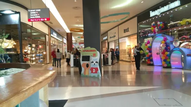 A tiled mall corridor with shopfronts, a colorful balloon arch and visitors
