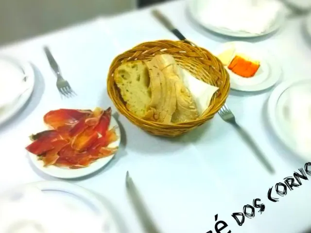 A bread basket on a white cloth beside a plate of thin cured meat slices