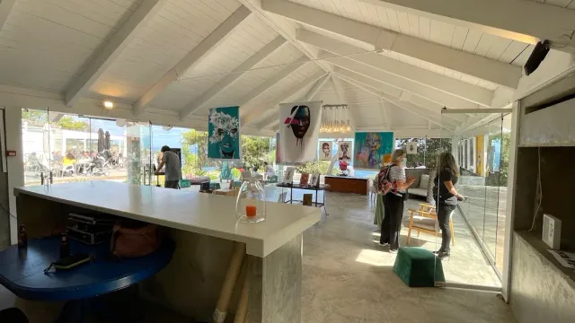 A white hall with wooden ceiling beams, paintings on the walls and visitors browsing