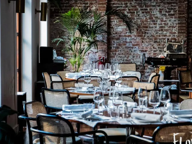 Tables set with wine glasses facing an exposed brick wall and cane chairs