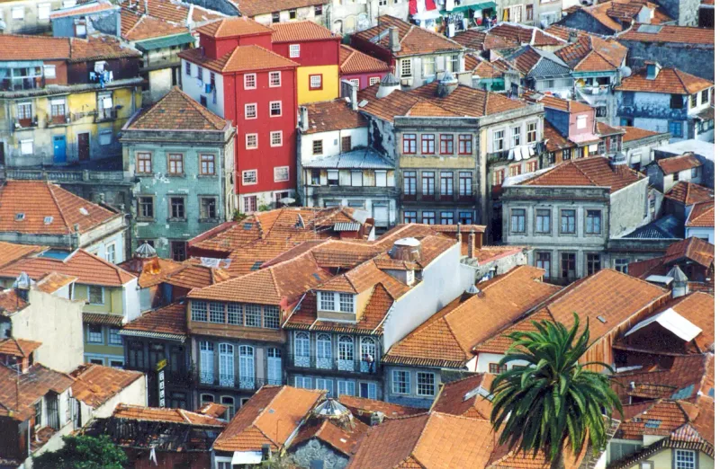 Aerial view over a dense jumble of orange tiled roofs and colourful house fronts