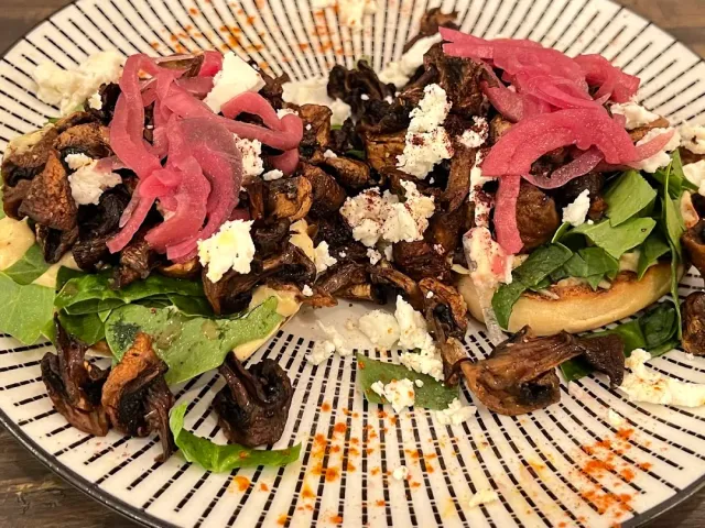 A striped plate with roasted mushrooms, pickled red onion, white cheese and salad leaves
