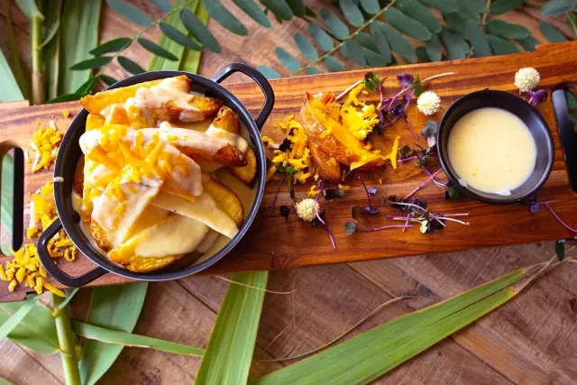 Fries with melted cheese in a small pot on a wooden board beside a sauce