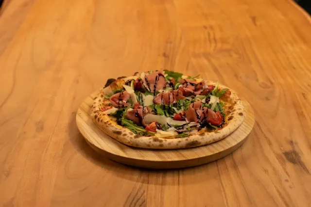 A pizza with pieces of meat, leaves and a dark sauce on a round wooden board