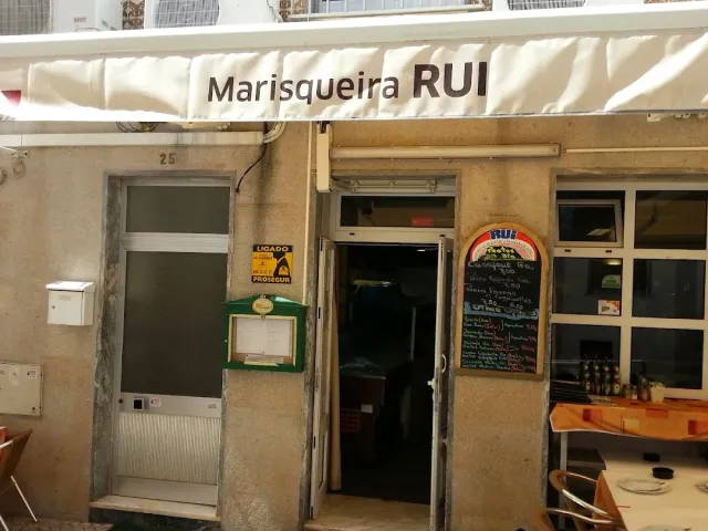 A facade with a white awning, a colourful chalkboard by the door and a table outside