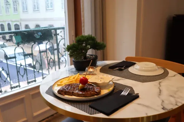 A steak plate with fries and sauce on a marble table by a balcony window
