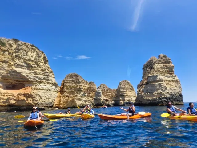 Yellow and orange kayaks on blue water at the foot of golden rock cliffs