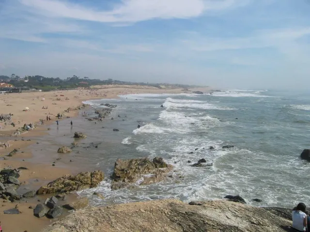 A wide sandy beach with dark rocks and white breaking waves