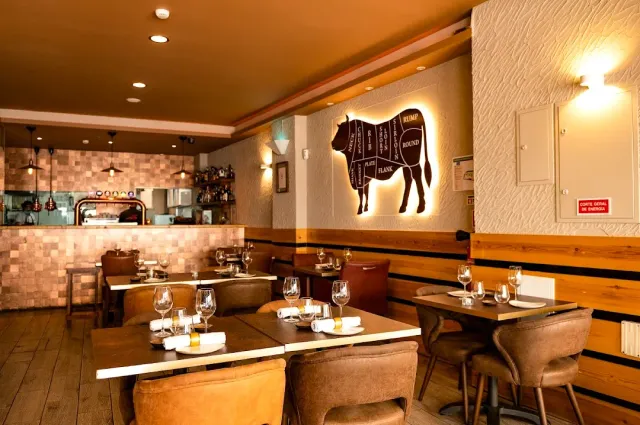A room with an illuminated cow diagram on the wall, leather armchairs and an open kitchen behind