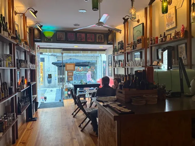 A narrow shop with beer bottle shelves, a wooden floor and a door open to the street