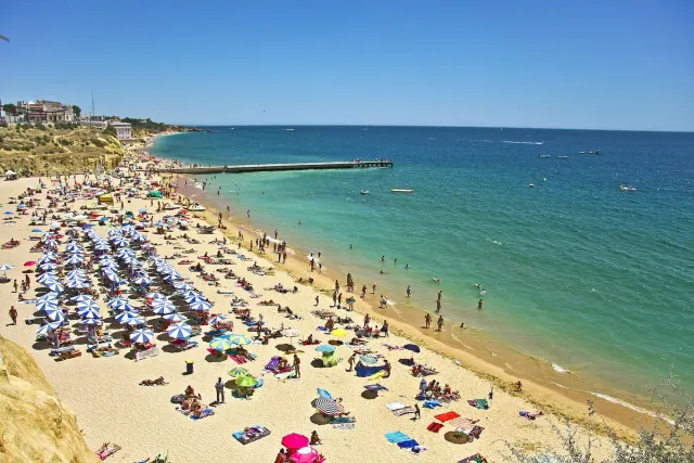 A beach packed with colourful parasols beside green and turquoise water