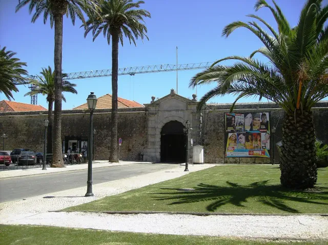 A stone gate in a low fortress wall with palms and lawn
