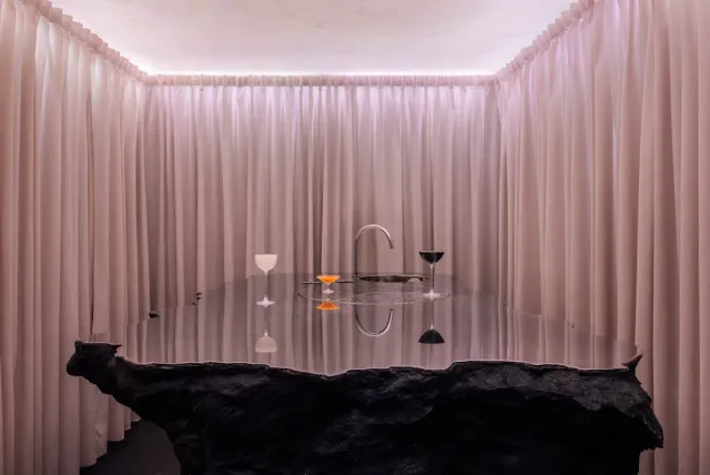 A room wrapped in pink curtains with a dark glossy counter and two cocktail glasses