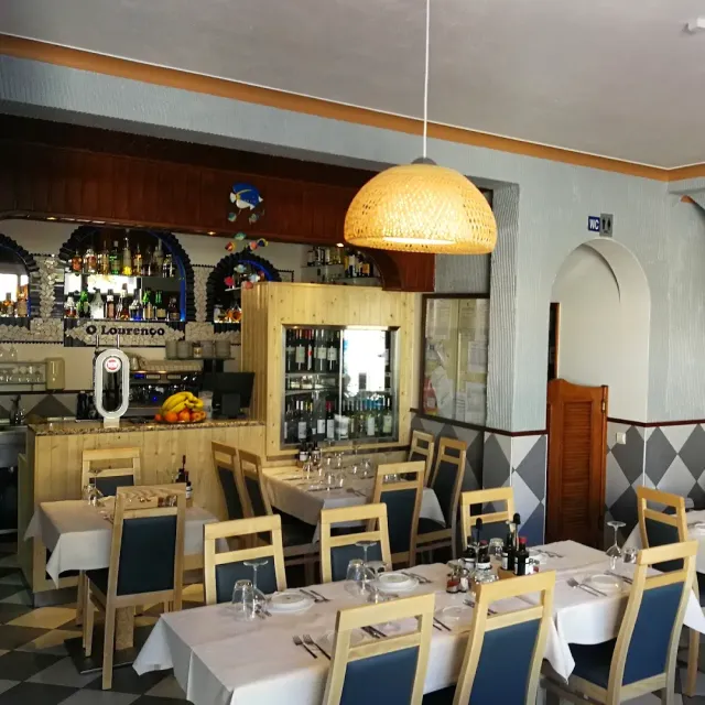 A room with a bottle bar, a large wicker lamp and tables with blue chairs