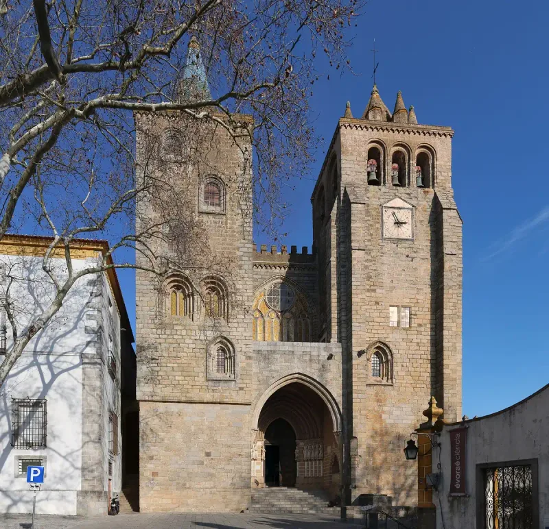 A granite cathedral front with two bell towers and a pointed entrance arch against a blue sky