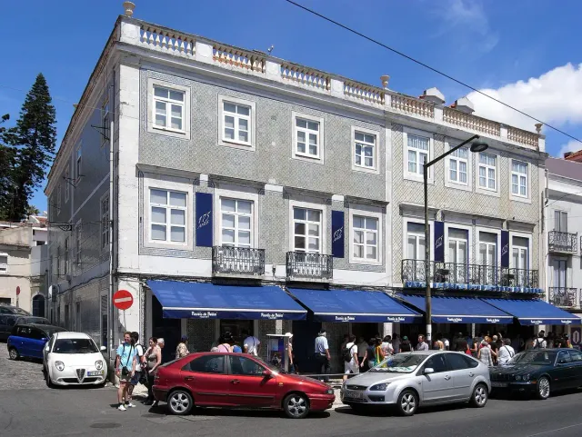 A long shop front with blue awnings and a crowd outside