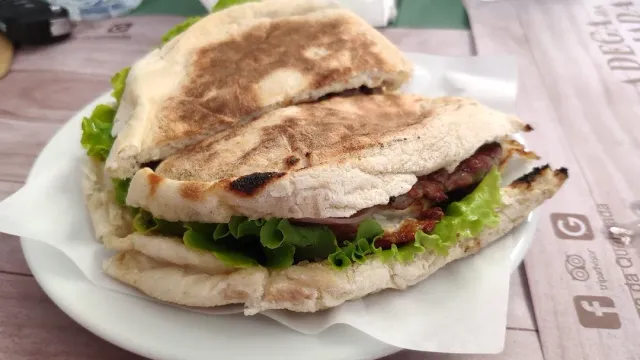 A sandwich in toasted flatbread with pieces of meat and lettuce leaves on a plate
