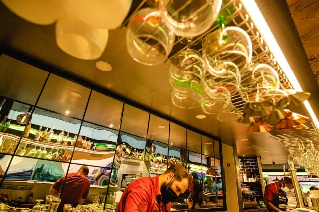 A bar in warm light with rows of hanging glasses and staff behind the counter