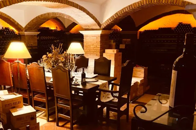 A brick vaulted wine cellar with a laid table, wooden chairs and lit bottle racks