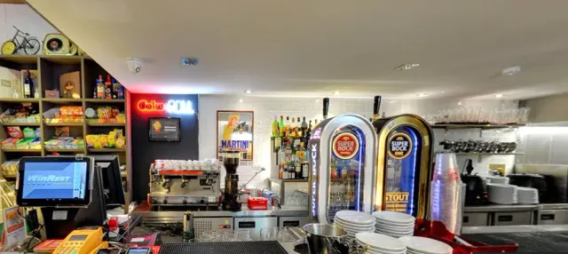 A counter with beer taps, a coffee machine, stacks of plates and shelves of snacks