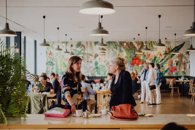A hall with industrial lamps, a tropical mural and diners at the tables