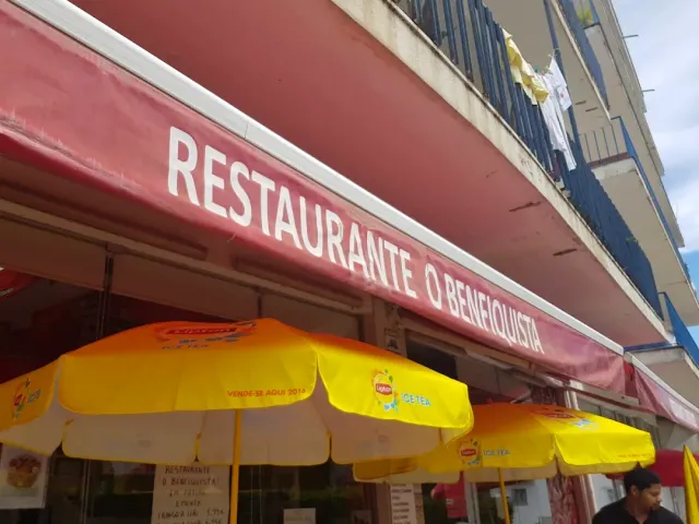 A large red awning above a facade, and below it a row of open yellow parasols
