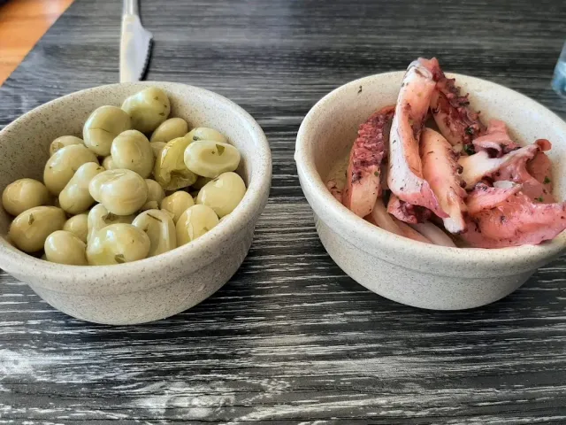 Two clay bowls on a dark table, one of potatoes and one of octopus