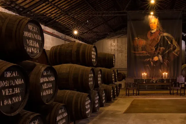 A cellar of stacked wooden barrels facing a large portrait banner and lit candelabra