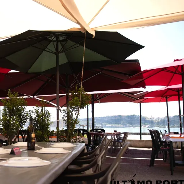 A terrace with red and green parasols and set tables facing the wide river