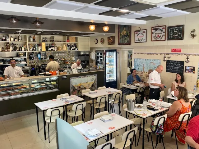 A busy space with a display counter, white tables and diners along the wall