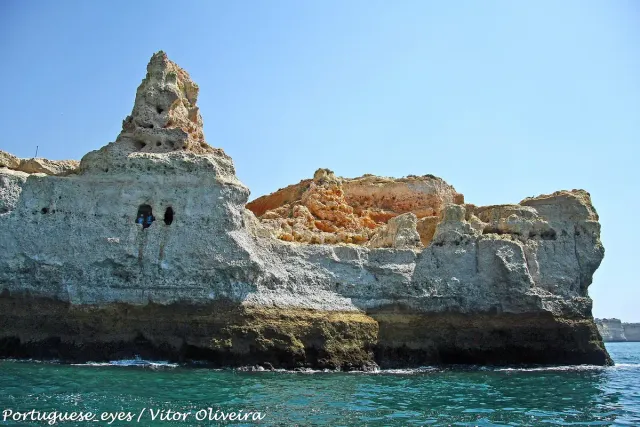 A sculpted limestone cliff with sea caves above clear green water