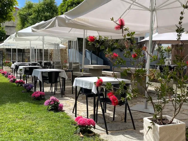 A garden with white parasols, white clothed tables and pots of pink flowers on the lawn