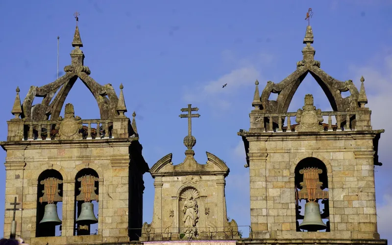 Two baroque bell towers with bronze bells and a stone cross between them