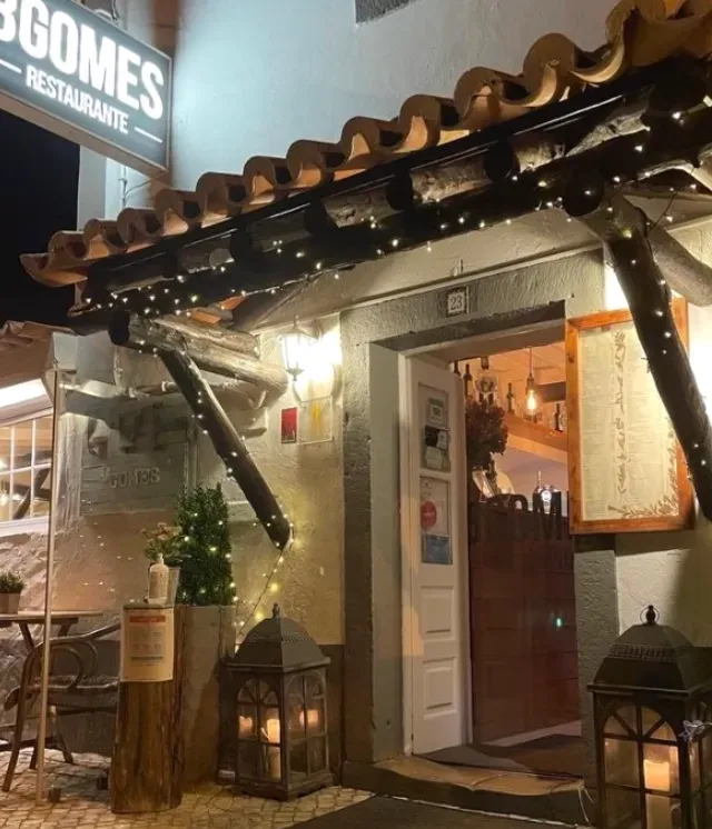 An entrance at night with a wooden canopy, a string of small lights and lit lanterns on the floor