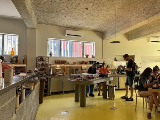 A space with a yellow floor, a concrete ceiling, a central counter with a display case, staff and customers