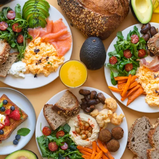 An overhead view of brunch plates with eggs, salmon, salads and orange juice