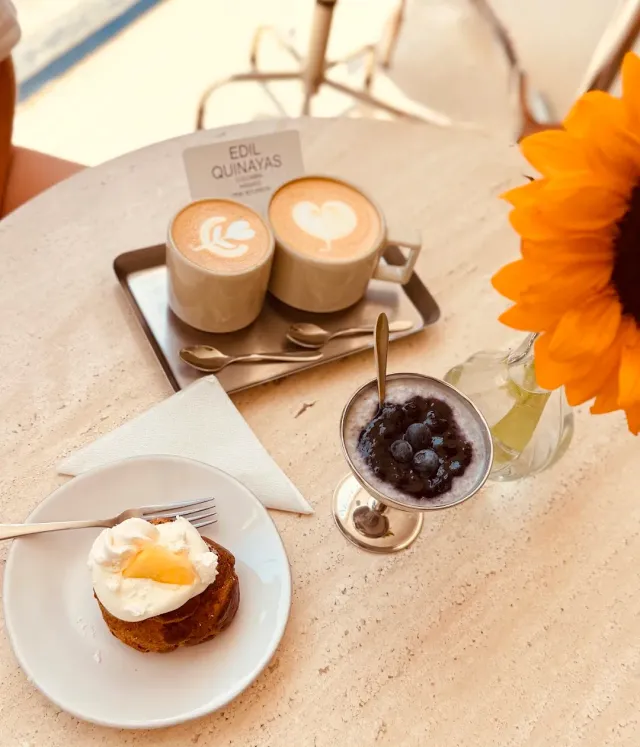 A stone table with two cups of coffee, a cake with cream, a blueberry dessert and a sunflower