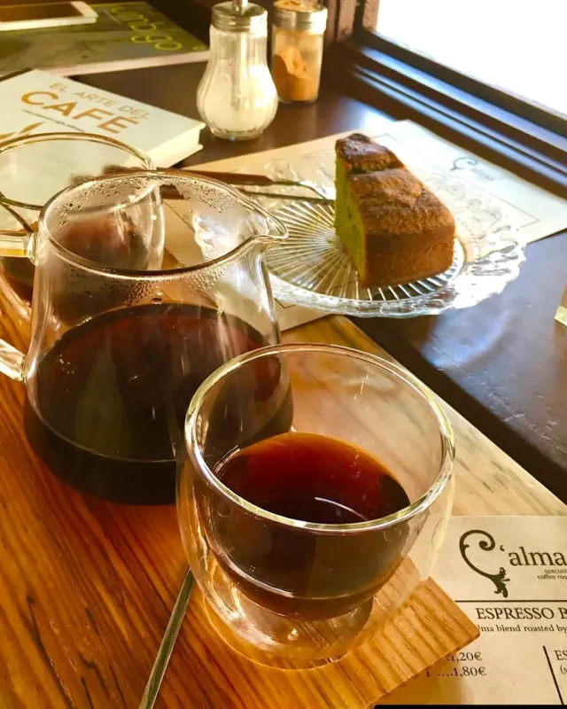 A glass carafe and a double-walled glass with filter coffee, beside a slice of cake