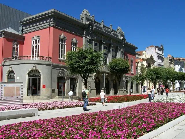 A historic theatre front facing pink flower beds and trees