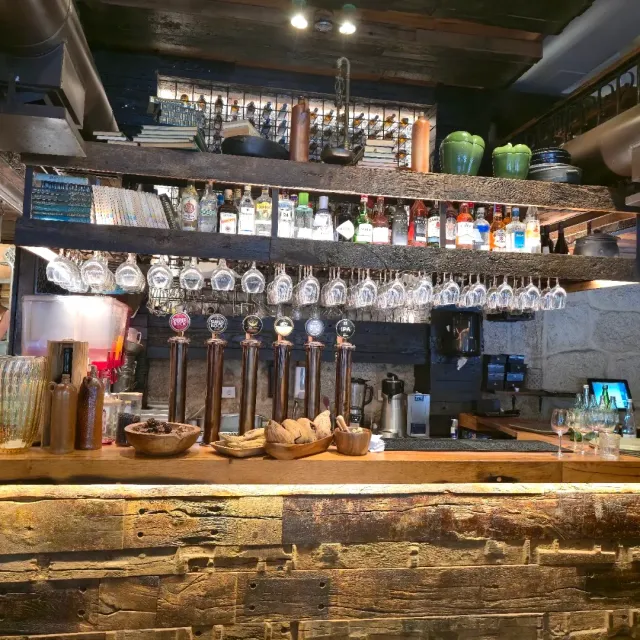 A bar counter with beer taps, hanging glasses and a bottle shelf on raw wood