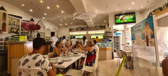 A space full of diners at white tables facing an open counter and shelves of bottles