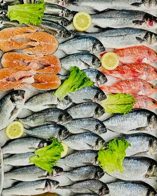 A display of fresh fish arranged in rows with salmon slices, lemon and lettuce leaves