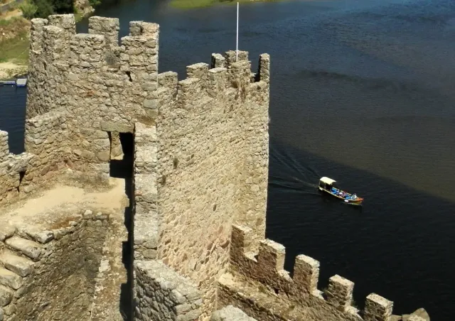 Crenellated walls and towers above a wide river with a small boat