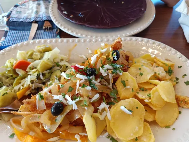 A plate with fish, fried onion, black olives, potato slices and pickled greens