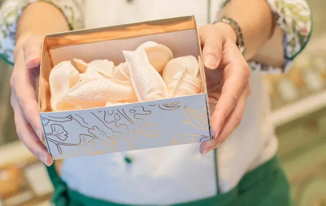 Hands holding an open card box filled with pale egg sweets