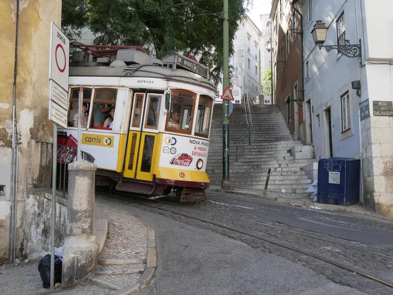 An old yellow tram climbing a narrow street between houses and stone steps