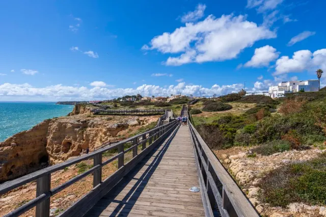 A boardwalk with a wooden railing along golden cliffs above a turquoise sea