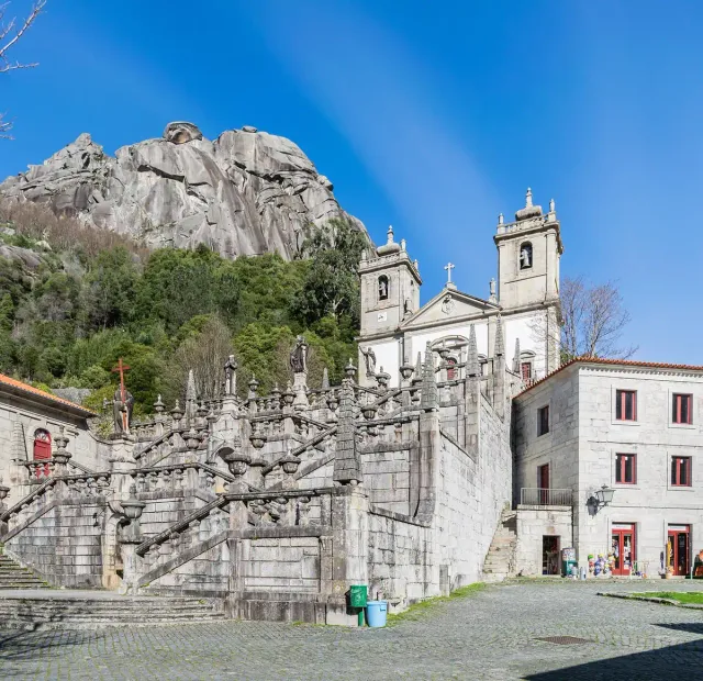 A white shrine with two towers and a monumental staircase below a rock face