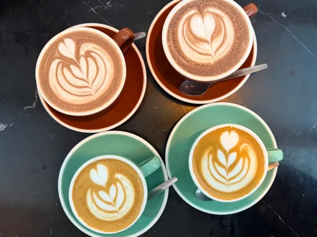 Four cups of coffee with foam art, on terracotta and mint saucers on dark marble