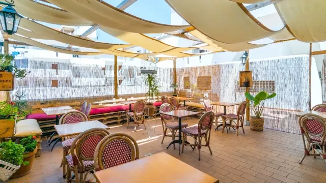 A courtyard covered with fabric sheets, wicker chairs, red benches and reed screens